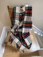Checkered wool shoulder warmer/throw draped over a wooden chair showing the color pattern and fringed ends.