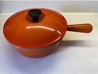 Front perspective of flame orange enameled cast iron pot with lid and side handle.
