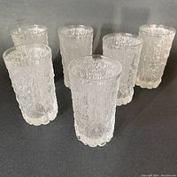 Six clear tumblers with an icy bark textured finish arranged on a dark surface showing overall shape and texture details.