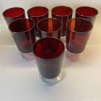 Eight ruby red water/red wine glasses arranged in a group showing the color, shape and clear stems/feet.