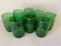 Eight small green glasses arranged in two rows on a white surface showing the cylindrical shape and consistent color.