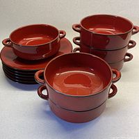 Front views showing six stackable handled bowls alongside six fitted plates in cherry red with black rim.