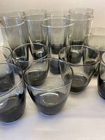 Set of 8 lowball and 8 highball smoky grey glasses arranged on a white surface