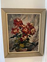 Frontal view of signed oil painting depicting muted red floral cluster in vase with muted grey, blue, and green background in textured frame.