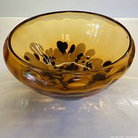 Side perspective of amber blown glass bowl showing curvature and decorative dark drips inside the bottom.