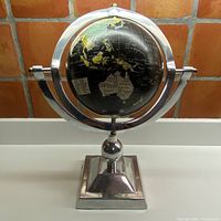 Front view of entire vintage globe on polished metal revolving stand showing globe centered in metal rings.