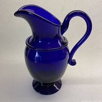 Full front and side view of the deep blue glass handled pitcher showing overall shape and design.