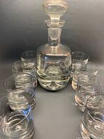 Photo showing the decanter surrounded by 8 matching lowball glasses, all clear crystal with visible bubbles in the thick bottoms.