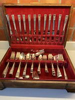 Full set displayed inside an open wooden box with red velvet lining showing all flatware and serving utensils organized by type.