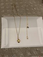 Two gold necklaces on white background showing twisted rope chain with heart pendant at left and fine cable chain at right