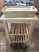 Kitchen cart with two slatted shelves and wooden top, with the wooden tray, acrylic cutting board, and wood cutting board stacked on top