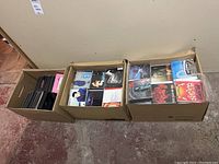 Top view of two cardboard boxes filled with jewel cases and DVD cases containing music CDs and DVDs, arranged in rows.