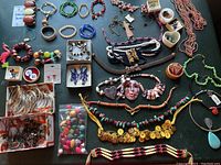 Wide view of assorted costume jewelry spread out on black surface showing necklaces, bangles, brooches, rings, earrings, and loose beads.