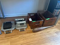 Full view of all items including two wooden crates, a wood juggling bat, and four metal CD/DVD cases on a wood floor.