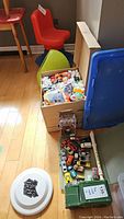 Overview photo showing die cast cars on tray, Playmobil figures in boxes, two chairs, and a frisbee on the floor.