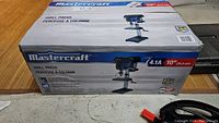 Photo showing the sealed Mastercraft drill press box with branding and model info visible.