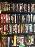 Four shelves of assorted DVD and Blu-ray cases arranged on a black bookshelf.