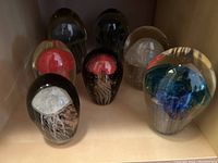 Seven handmade glass jellyfish paperweights on shelf, varying in colors and shapes.
