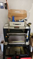 Front view of Mastercraft thickness planer on stand with cardboard box of pocket hole jig and clamp on top