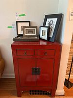 Front view of red lacquered side table cabinet with picture frames on top.