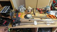 View of entire workbench with air compressor, hand saw, grinding stone, clamps, and various other tools and hardware items.