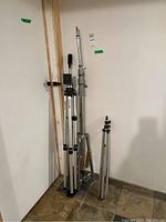 Three aluminum tripods standing upright against a wall, including one with caster wheels and one smaller tripod.