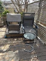 Two zero gravity chairs and one round side table on a wooden deck.