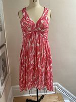 Full front view of sleeveless pink and white sleeveless summer dress with pleats below bust on a mannequin.