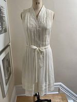 Front full view of the lightweight sleeveless dress on a dress form showing pleats, buttons, and tie belt.