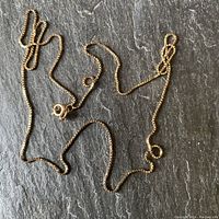 Full view of the gold box chain necklace laid out on slate background showing entire length and clasp.