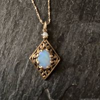 Close-up of diamond-shaped filigree pendant showcasing oval opal and seed pearl