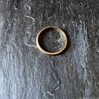 Plain 14K gold wedding band lying flat on a textured dark surface, shows smooth gold finish and wear marks.