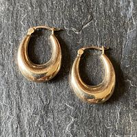 Pair of yellow gold hoop earrings displayed on a dark textured surface, showing front view and clasp.