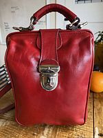 Front view of red leather bag with top handle and silver clasp lock showing brand logo Cecile Jeanne.