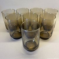 Front angled view of seven smoky brown tumblers arranged in a rough circle showing their translucent gradient from light to dark brown glass.