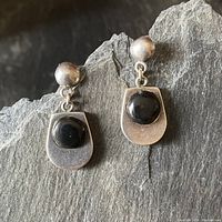 Pair of mid-century sterling silver drop earrings with black onyx centers placed on dark stone background to show overall design.