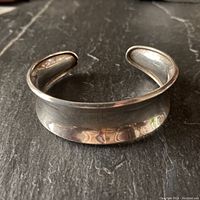 Sterling silver concave cuff bracelet with rolled edges and lightly curved profile, showing front view on dark surface.