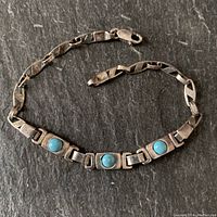 Full view of sterling silver bracelet with three round turquoise stones in rectangular bezels, closed clasp visible.