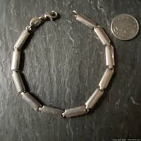 Full view of the Fossil sterling silver bracelet laid flat alongside a coin for size comparison. Bracelet consists of a series of solid rectangular silver links connected by rings and a lobster clasp closure.