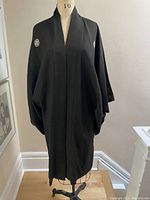 Full front view of the black vintage kimono on a dress form showing the wide sleeves and the body falling to below the knee.