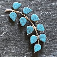 Photo showing entire pin with turquoise leaves on sterling silver branch against dark textured background to highlight details