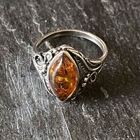 Close-up of the sterling silver ring showing the marquise-shaped amber stone and the intricate leafy and scroll border design.