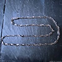 Full length view of twisted and concave sterling silver chain necklace on black background.