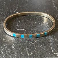 Front angle of the oval silver bracelet with turquoise inlays on black surface showing band and stones.