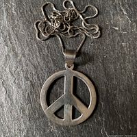 Photo of the pendant and chain laid on dark surface showing the peace sign pendant with a round shape.