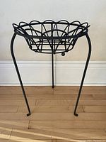 Front view of black wrought iron plant stand with removable bowl in place showing three legs and circular frame.