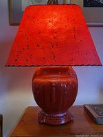 Full view of red glass lamp with glowing red shade on wooden surface