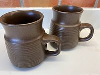 Two milk chocolate brown Denby mugs side by side showing full profile and handle design.