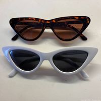 Top view of both pairs of cat eye horn rimmed sunglasses, one white and one tortoise shell.