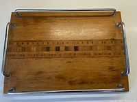 Top view of a rectangular wooden tray with chrome handles on all sides and wood inlay detail in the center.
